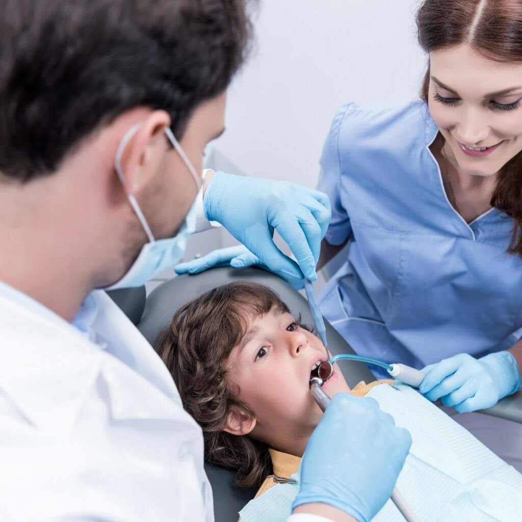 dentists treating teeth of little patient in dentist chair in hospital