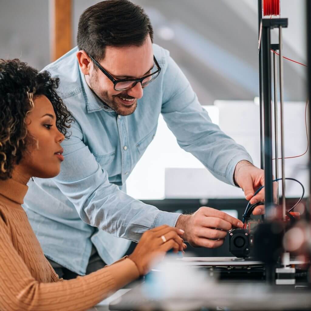 Technology, people and engineering concept. Handsome man learning woman how to use 3D printer.